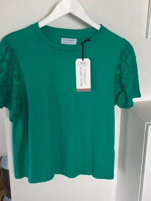 Holly & Whyte LindexM Ny!! med broderi anglaise-detaljer!  - Kortärmad topp med broderi anglaise-detaljer från Holly & Whyte Lindex M Ny med prislapp    Rund halsringning Korta ärmar Innehåller 80% ekologisk bomull Innehåller 20% återvunnen bomull Längd 57 cm i storlek M Axel t axel cirka 38 cm   Nypris 299    