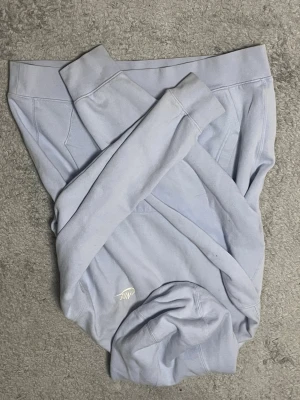 Ljusblå hoodie från Nike - Snygg ljusblå hoodie från Nike med klassisk logga broderad framtill. Hoodien har huva och ribbade muddar vid ärmslut och nederkant. Tillverkad i mjukt bomullsmaterial som känns skönt mot huden. Perfekt för en avslappnad och sportig stil.
