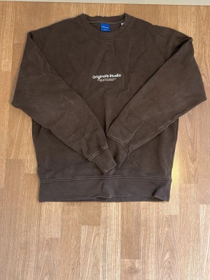 Brun sweatshirt Originals Studio - Mörkbrun sweatshirt från Originals Studio med rund halsringning och tryckt vit text på bröstet. Tröjan har ribbade muddar vid ärmslut och nederkant. Perfekt nu inför hösten och vintern. Tveka inte på att höra av dig vid funderingar!✨