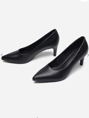 Svarta klassiska pumps med spetsig tå - Stilrena svarta pumps med spetsig tå och låg klack. Skorna är tillverkade i slätt konstläder och har en elegant siluett som passar till många olika looks. Perfekta för dig som gillar en tidlös och chic stil.