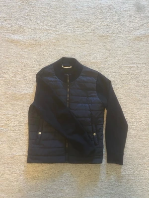 Sayless cardigan  - Stilren marinblå  cardiganjacka med quiltat framstycke och släta ärmar. Jackan har dragkedja framtill, två fickor med tryckknapp och ribbad krage. Perfekt för lager-på-lager och ger en sportig men ändå clean look.
