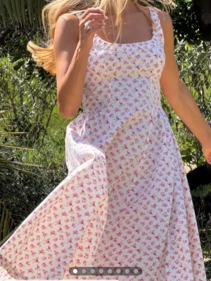 Vit långklänning med blommigt mönster - Romantisk långklänning i vitt med små rosa blommor och breda axelband. Klänningen har smock i ryggen och en luftig, svepande kjol. Perfekt för varma dagar och somriga tillfällen. Är enbart provad, men lappen har ramlat av!💞kom inte till användning! Nypris 699