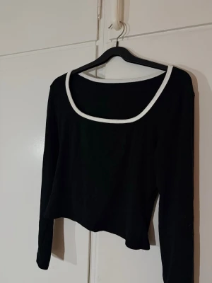 Svart långärmad topp med vit kant - En svart långärmad topp med vit kant runt den fyrkantiga ringningen. Toppen har en croppad passform och är i ett mjukt material. Perfekt med höga jeans eller kjol. Använd 2 gånger. Storlek L men passar M också. 