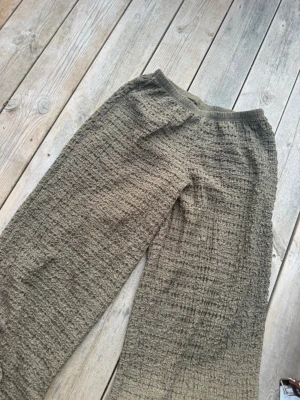 Olivgröna byxor  - Säljer ett par olivgröna mjukisbyxor med resår i midjan och avslappnad passform. Byxorna har en unik rutmönstrad struktur i tyget som ger en cool och trendig vibe. Perfekta för chill dagar eller när du vill vara bekväm men ändå se snygg ut.