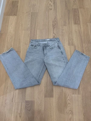 Ljusgrå raka jeans med rå kant - Säljer ett par ljusgrå jeans med rak passform och råa, fransiga benslut. Klassisk femficksmodell och hög midja. Jeansen är i ett mjukt denimtyg som ger en avslappnad vibe och passar perfekt till sneakers eller boots.