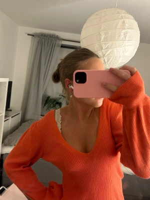 Ribbad tröja från Vila - Trendig ribbad tröja från Vila med V-ringning och långa, lätt puffiga ärmar. Den är mer korall färgad och inte orange som den ser ut att vara på bilden. Materialet är stretchigt och mjukt, perfekt för en snygg och bekväm look. Passar perfekt till jeans eller kjol för en färgstark outfit. 
