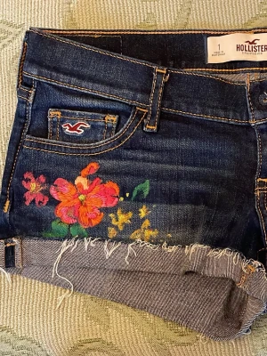 Jeansshorts från Hollister med blomdetalj - Mörkblå jeansshorts från Hollister med broderade blommor.