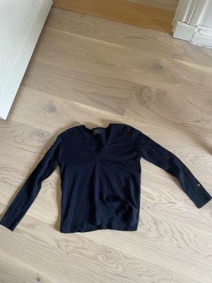 Svart stickad tröja med V-ringning - En enkel och stilren svart stickad tröja med V-ringning och långa ärmar. Tröjan har en smal passform och är tillverkad i ett mjukt, tunt material som passar perfekt till lager på lager. Klassisk modell utan synliga detaljer.