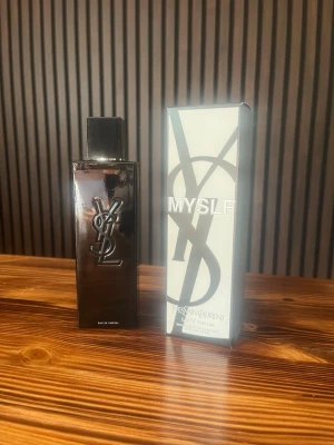 YSL MYSLF Eau de Parfum - Säljer en YSL MYSLF Eau de Parfum. Flaskan är rektangulär och svart med en blank finish och har den ikoniska YSL-loggan i silver på framsidan. Kommer med originalkartong i vitt och svart med stor logotyp. Perfekt för dig som gillar exklusiva dofter. Helt oanvänd! Skriv vid frågor