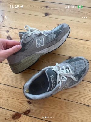 Grå New Balance 990 sneakers - Klassiska New Balance 990 sneakers i grått med vita detaljer och snörning. Ovandelen är i mesh och mocka för en sportig look. Tjock sula i grå och svart, samt tydlig New Balance-logga på sidan och tungan. Perfekta för dig som gillar retrostil.