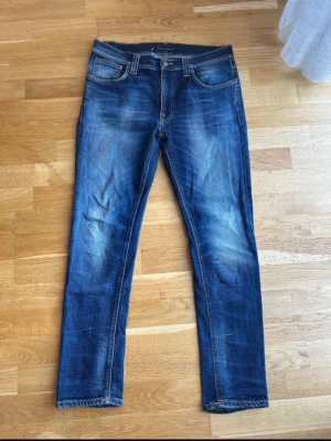  Nudie Jeans - Säljer ett par klassiska blå slim fit jeans från Nudie Jeans med snygga slitningar och femficksmodell. Jeansen har normal midja, dragkedja och knappstängning samt kontrastsömmar. Perfekta till en avslappnad stil. Model lean deen.