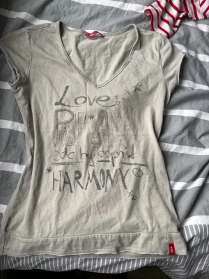 t-shirt med tryck - Snygg  t-shirt  med v-ringning och korta ärmar. Framsidan har ett coolt tryck med texten 'Love, Peace, Harmony' och små detaljer. Tillverkad i mjukt bomullsmaterial som känns skönt mot huden. Perfekt till jeans eller shorts.