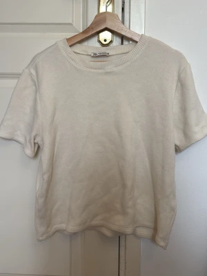 Beige stickad topp med kort ärm - En enkel och stilren beige stickad topp med rund halsringning och korta ärmar. Perfekt till jeans eller kjol för en clean look. Mjuk och skön kvalitet som känns lyxig mot huden. XL men passar som S
