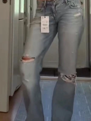 Ljusblå slitna raka jeans - Säljer ett par helt nya ljusblå jeans med raka ben och slitningar vid knäna och låret. Jeansen har klassisk femficksmodell och hög midja. Perfekta för en avslappnad och trendig look. Trendiga och slutsålda!