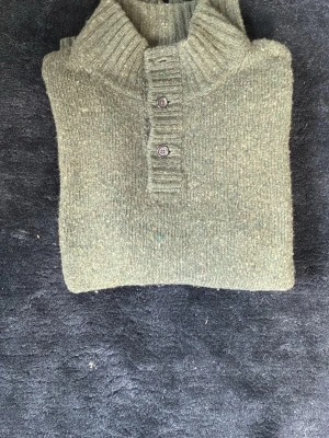 Olivgrön stickad tröja med knappar från polo Ralph lauren - Mysig olivgrön stickad tröja med hög krage och två knappar framtill. Tröjan har långa ärmar och ribbstickade muddar vid ärmslut och nederkant. Perfekt för kalla dagar och enkel att styla till olika outfits.