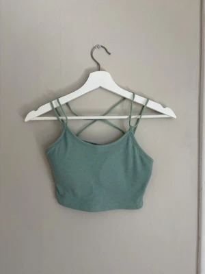 Ribbad grön crop top med smala band - Snygg ribbad crop top i ljusgrönt med tunna axelband som korsas i ryggen. Toppen har en tight passform och är gjord i ett stretchigt material som känns bekvämt mot huden. Perfekt till sommaren eller för lager på lager-stil.