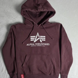 Alpha Industries hoodie vinröd storlek S - Klassisk Alpha Industries hoodie i vinröd/lila nyans med stort logotryck framtill och ikonisk “Remove Before Flight”-tagg. Tjock och mjuk fleecefodrad modell i mycket bra skick. Perfekt streetwear/Y2K-plagg.  Storlek S Normal passform  Gott skick, se bilder  Mått Bröstbredd: ca 53 cm Plagglängd: ca 63 cm Axelbredd: ca 44 cm Armlängd: ca 60 cm  Material 80% bomull 20% polyester  Tycker du priset är för högt? Skicka ett prisförslag!