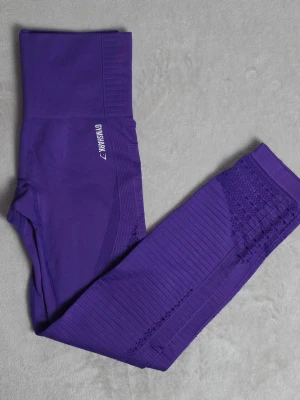 Gymshark seamless träningstights – lila – XS – nyskick - Snygga och bekväma seamless tights från Gymshark i en stark lila färg. Hög midja med kompression och stretchigt material som sitter väldigt bra på kroppen. Ventilerande detaljer längs benen och vid anklarna.  Använda endast en gång – i princip nyskick.  Storlek: XS Färg: Lila Material: 93% nylon / 7% elastane Modell: Seamless / high waist  Mått ungefär:  • Midja platt: ca 28 cm • Grenhöjd/front rise: ca 25 cm • Innerbenslängd: ca 60 cm • Benöppning: ca 10 cm