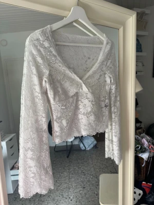 Vit spetsblus med v-ringning - Säljer en superfin vit blus i spets med v-ringad hals och långa ärmar. Blusen är croppad och har en romantisk känsla med genombrutet spetsmönster. Perfekt att styla med jeans eller kjol för en trendig look.