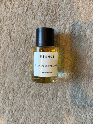 ESSNCE Strawberry Eclair parfym - En parfym från ESSNCE med doften Strawberry Eclair. Flaskan är cylindrisk i genomskinligt glas med svart lock och vit etikett med enkel text. Innehållet är bärnstensfärgat och ger ett fräscht och modernt intryck. Perfekt för dig som gillar söta och fruktiga dofter.