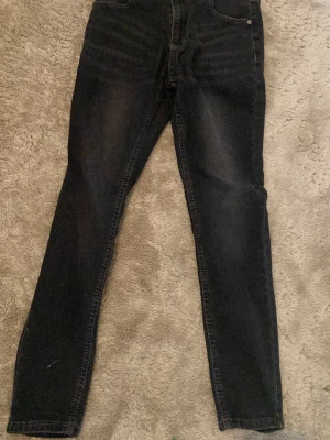 Svarta skinny jeans med hög midja - Säljer ett par svarta skinny jeans med hög midja och klassisk femficksdesign. Jeansen har en lätt tvättad look och smal passform hela vägen ner. Perfekta till en avslappnad streetstyle. Materialet är troligtvis bomull med stretch.