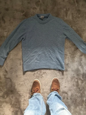 Ljusblå stickad tröja - En stilren ljusblå stickad tröja med rund halsringning och ribbade muddar vid ärmslut och nederkant. Perfekt för lager på lager och enkel att matcha med jeans eller chinos. Tröjan har en klassisk passform och är mjuk i materialet.