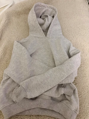 Ljusgrå hoodie med huva XS - En basic ljusgrå hoodie i mjukt sweatshirtmaterial. Hoodien har en klassisk huva, ribbade muddar vid ärmslut och nederkant samt en magficka framtill. Perfekt för en avslappnad och stilren look.