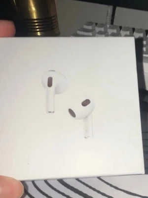 Airpods Gen 3 - Säljer ett par vita Airpods gen 3  hörlurar med stilren design och laddningsetui. Hörlurarna har en slimmad form och sitter bekvämt i öronen. Perfekta för musik, poddar och samtal. Laddningsetuiet är kompakt och lätt att ta med.