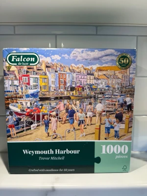Falcon de luxe pussel Weymouth Harbour - Säljer ett pussel med 1000 bitar från Falcon de luxe med motivet Weymouth Harbour av Trevor Mitchell. Färgglad bild av en hamn med båtar, människor och klassiska brittiska hus. Perfekt för dig som gillar utmanande pussel och vackra motiv. Helt nytt i originalkartong.