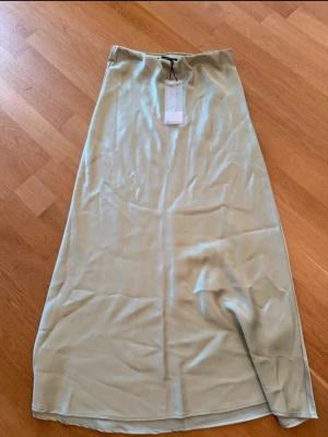 Ljusgrön långkjol i satin - Säljer en stilren ljusgrön långkjol i satin med slät yta och lätt glans. Kjolen har en enkel, rak passform och är perfekt för dig som gillar minimalistisk stil. Supersnygg att matcha med både sneakers och klackar.