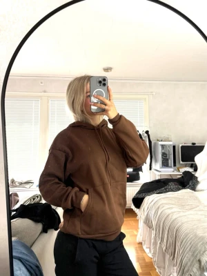 Brun hoodie med huva - Säljer en enkel och snygg brun hoodie med huva och känguruficka framtill. Hoodien har en avslappnad passform och ribbade muddar vid ärmslut och nederkant. Perfekt för chill dagar eller när du vill ha något bekvämt och stilrent.