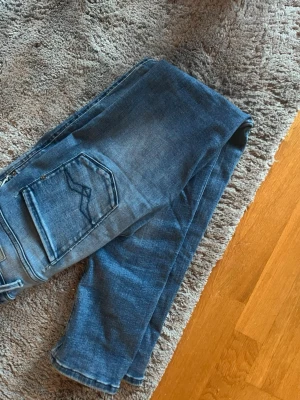Blå Replay jeans Anbass W29 L32 - Säljer ett par blå jeans från Replay det är slim fit och har en  klassisk femficksdesign. Jeansen har snygga slitningar och en cool tvätt som ger en avslappnad look. Perfekta till vardagsstilen och passar till det mesta. Materialet är mjukt denim för skön känsla. Det fins små hål som syns på bilderna men det är inget som syns när du har på dem hojta bara till om ni undrar något🙌😁