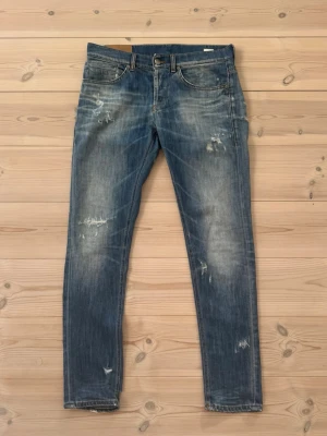 Dondup jeans - Säljer ett par blå dondup jeans med slitningar och distressed detaljer på både fram- och baksida. Jeansen har klassisk femficksdesign och normal midja. Perfekta för en avslappnad och trendig look.