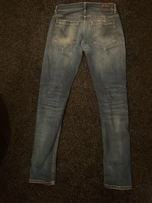 Blå slim fit jeans med slitningar - Snygga blå slim fit jeans med lätt slitna detaljer och tvättade partier på låren och knäna. Klassisk femficksmodell med dragkedja och knapp i midjan. Jeansen har smal passform och är tillverkade i denim med lite stretch för extra komfort.