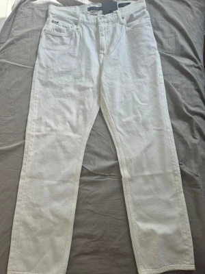 Vita Tommy Hilfiger Jeans - Säljer ett par vita jeans med rak passform och klassisk femficksdesign. Jeansen har bälteshällor och knappgylf. Materialet ser ut att vara denim i bomull. Perfekta för dig som vill ha en clean och stilren look.