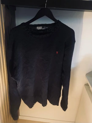Mörkblå stickad tröja Polo Ralph Lauren - Klassisk mörkblå stickad tröja från Polo Ralph Lauren i 100% bomull. Tröjan har rund halsringning, ribbade muddar och den ikoniska röda logotypen broderad på bröstet. Perfekt för en stilren och avslappnad look. Pris kan diskuteras vid snabb affär