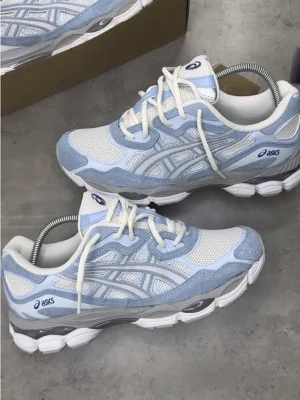 Helt nya ASICS vita och ljusblå sneakers - Säljer ett par fräscha ASICS sneakers i vitt och ljusblått. Skorna har mesh- och mockadetaljer, klassisk ASICS-logga på sidan och en chunky sula för extra komfort. Perfekta för dig som gillar sportig och trendig stil.