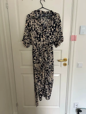 Beige och svart långklänning SHEIN - Säljer en långklänning från SHEIN med beige och svart leopardmönster. Klänningen har v-ringning, korta ärmar och markerad midja. Perfekt för dig som gillar statementplagg med coolt mönster.