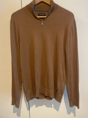 Brun halvzip tröja från Jack & Jones - Snygg brun tröja från Jack & Jones med halvzip och hög krage. Tillverkad i mjukt stickat material, perfekt för lager på lager. Långa ärmar och ribbade muddar ger en clean look. Enkel att matcha med jeans eller chinos.