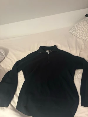 Mörkblå stickad tröja från Dobber - Mörkblå stickad tröja från Dobber med ribbad struktur och half zip-dragkedja framtill. Tröjan har lång ärm och hög krage, perfekt för kyligare dagar. Enkel och stilren design som passar till det mesta. Knappt använd 