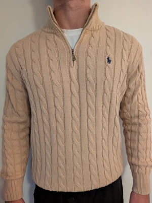 Ralph Lauren Polo kabelstickad tröja, beige, stl M - Ralph Lauren Polo kabelstickad tröja med kort dragkedja, beige, ponylogga på bröstet. Stl M. Klassisk collegestil som funkar året runt. Fint skick. Modell: 182cm | 83kg.