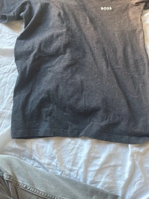 Mörkgrå t-shirt från BOSS - Snygg mörkgrå t-shirt från BOSS med diskret logga på bröstet. Klassisk passform och rund halsringning. Perfekt basplagg till garderoben och enkel att matcha med jeans eller shorts.