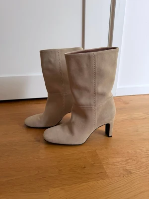 Beige stövletter med klack - Snygga beige stövletter i mockaimitation med medelhög klack. Stövletterna har en enkel och stilren design som passar till många olika outfits. 