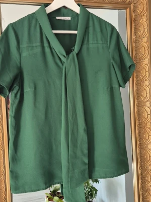 Grön blus med knyt i halsen - Stilren grön blus med korta ärmar och snygg knytning i halsen. I bra skick
