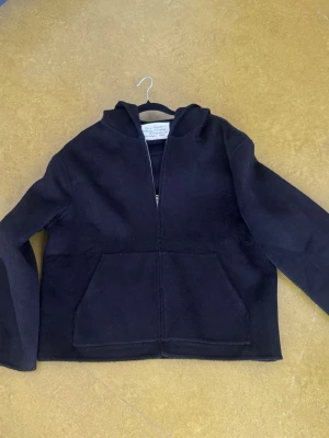 Acne Studios cashmere jacka  - Size S. Svart hoodie från Acne Studios med dragkedja framtill och stor känguruficka. Tillverkad i ett tjockare material som känns mjukt och lyxigt. Klassisk huva och stilren design, perfekt för en clean och avslappnad look.