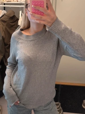Ljusgrå stickad tröja - En enkel och stilren ljusgrå stickad tröja med rund halsringning och ribbade muddar vid ärmslut och nederkant. Tröjan har en avslappnad passform och är perfekt för lager på lager. Kanske lite nopprig