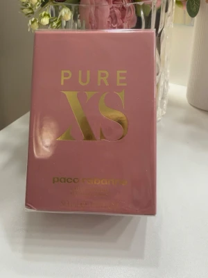 Paco rabanne pure XS for her- Eau de parfum 50ml - En feminin, söt och sensuell parfym med en varm och lyxig doft. Den har härliga noter av bland annat vanilj, popcorn, persika, apelsinblomma och ylang-ylang, med en varm och mjuk bas. O Helt ny och oöppnad i originalförpackning. 50 ml. Perfekt som present eller till dig själv!