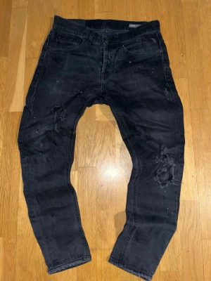 Dondup jeans - Säljer ett par svarta jeans med skinny fit och slitningar samt hål på benen. Jeansen har fem fickor, låg midja och detaljer som färgstänk och distressed look. Perfekta för en edgy streetstyle.