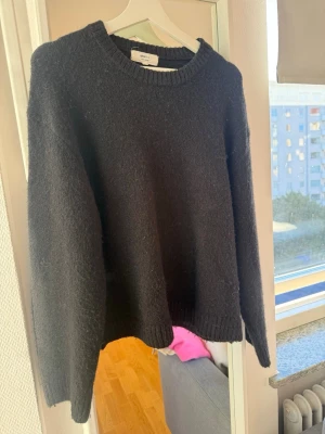Svart stickad tröja med rund hals - En klassisk svart stickad tröja med rund halsringning och ribbstickade muddar vid ärmslut och nederkant. Tröjan har en enkel och stilren design som passar perfekt till många olika outfits.