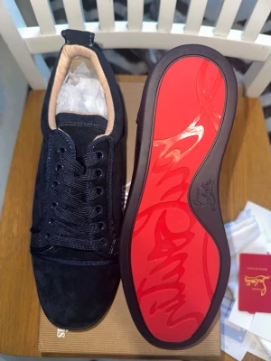 Mörkblåa Christian Louboutin sneakers - Snygga svarta sneakers från Christian Louboutin med klassisk röd sula och diskret logga. Skorna är låga och har ovandel i mocka med svarta skosnören och beige innerfoder. Perfekta för dig som vill ha en exklusiv och stilren look.